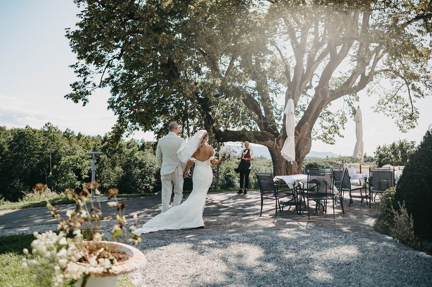 A couple shares an intimate moment during their outdoor wedding ceremony under a large tree at sunset.