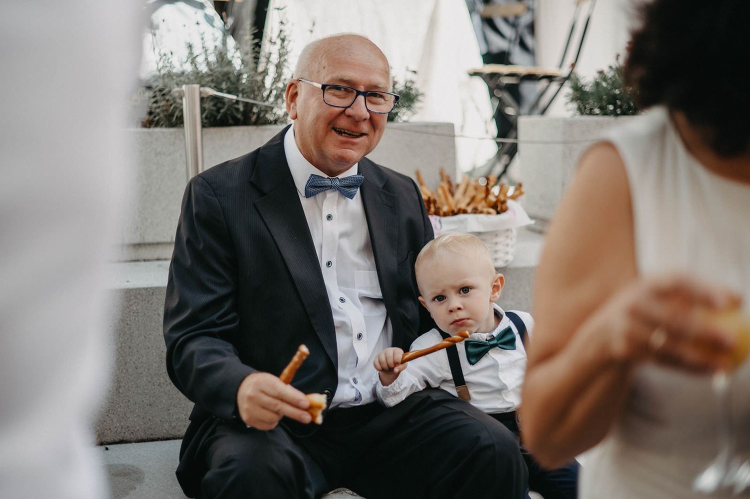 A black and white candid moment captured during a wedding reception shows guests sharing laughter and conversation.
