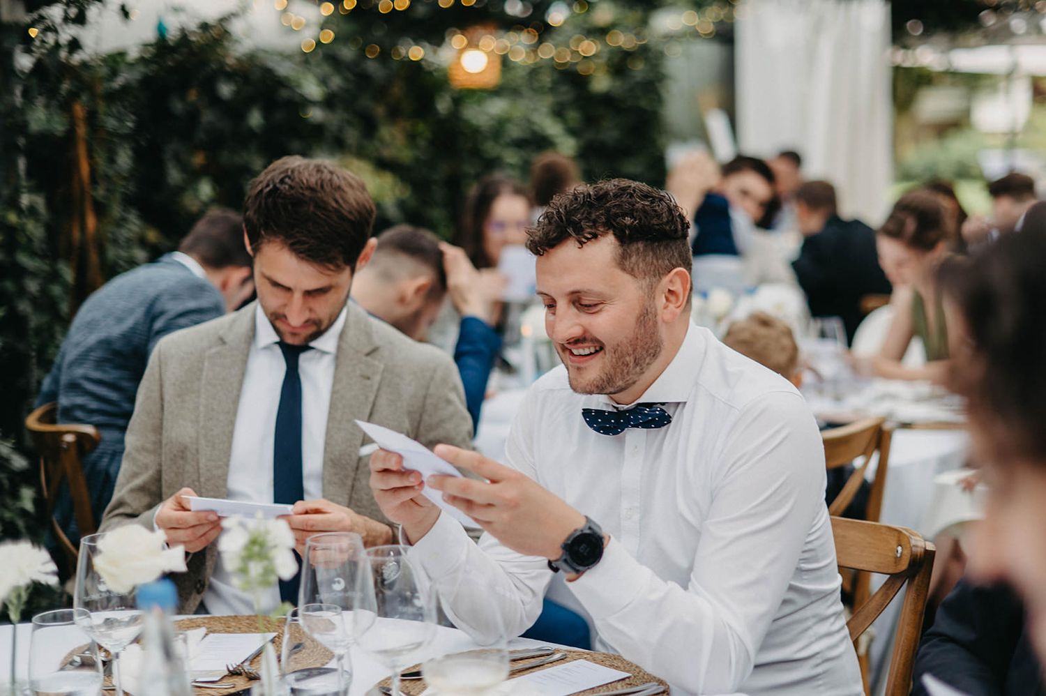 Wedding guests enjoy an elegant outdoor reception dinner at tables decorated with white linens and floral centerpieces.