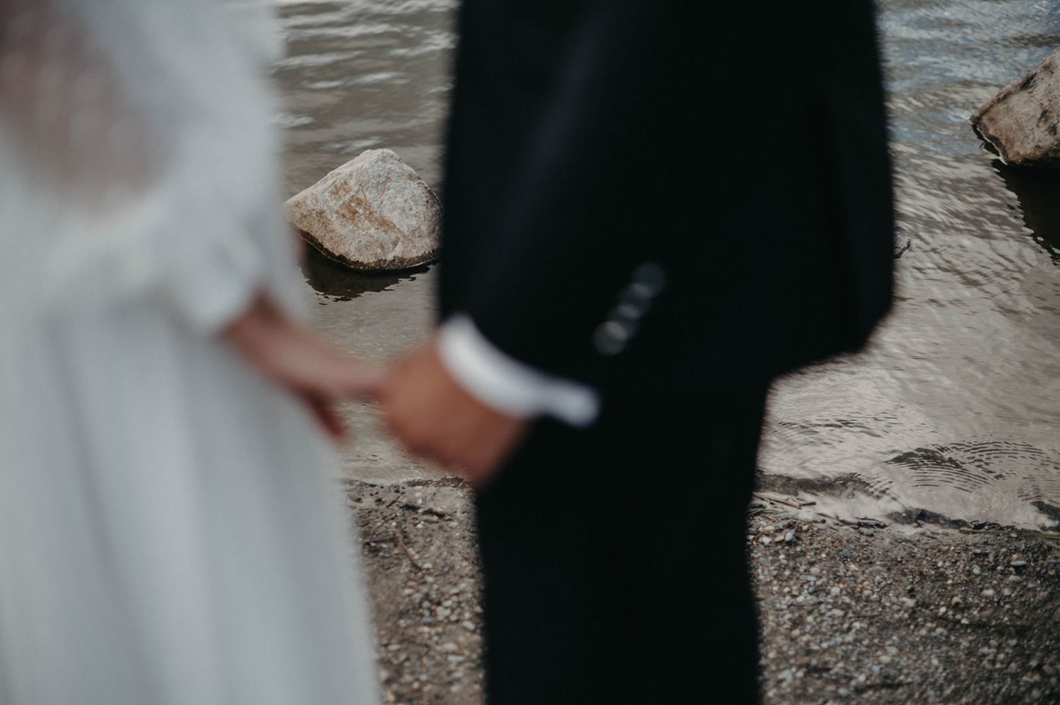 Close-up shot of a couple holding hands during their wedding ceremony against a textured wall background.