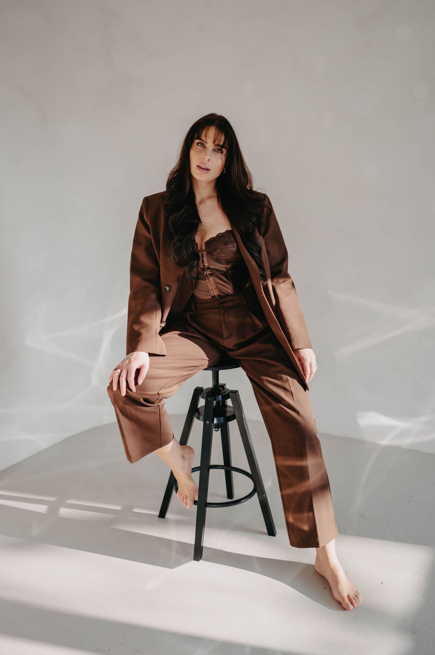 Stylish portrait in brown satin loungewear seated on a black stool.