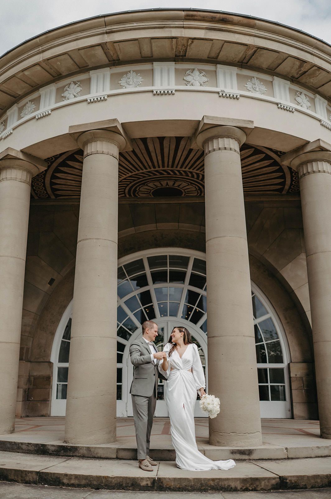 A grand neoclassical building entrance with elegant columns and arched windows creates a romantic backdrop.