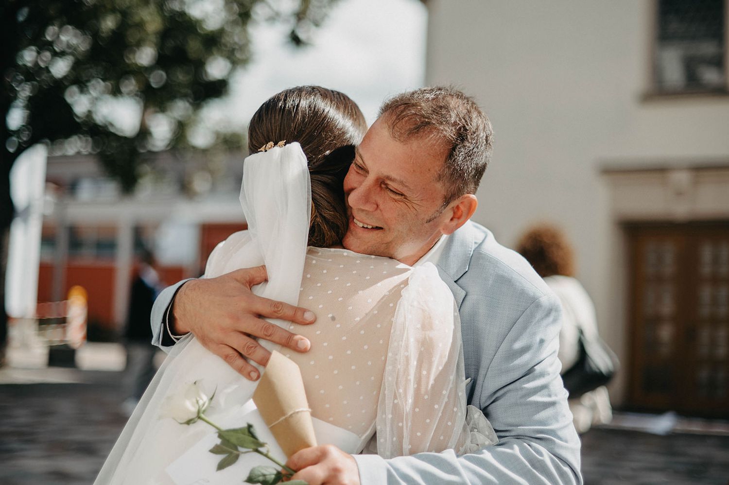 A couple in formal attire shares an intimate kiss outdoors in a romantic wedding setting.