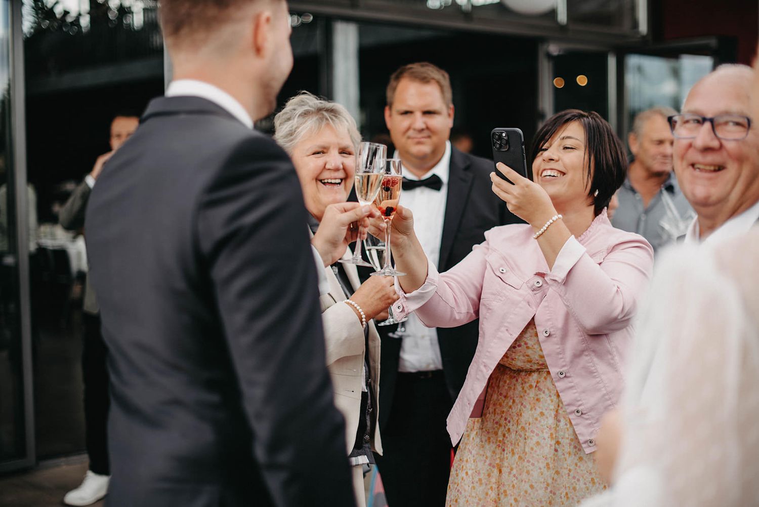 Group of wedding guests laughing and smiling together during an outdoor reception celebration.