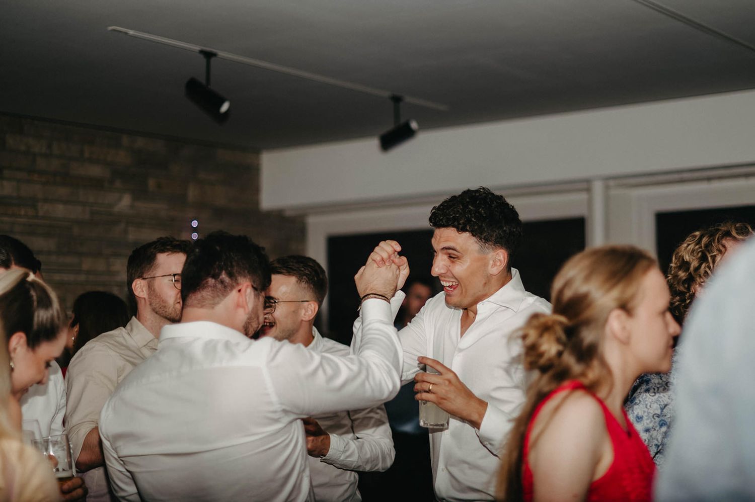 Wedding guests dance together in celebration during a reception party at an indoor venue.