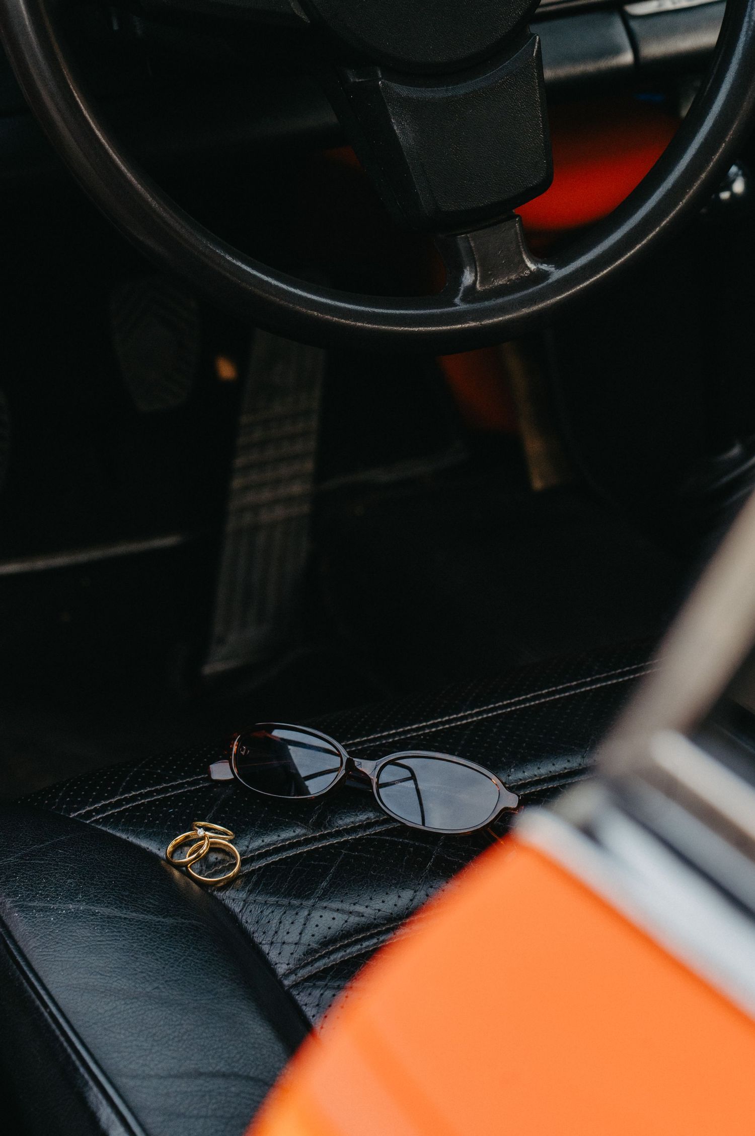 Close-up view of black leather car interior with orange accents and steering wheel visible in dark lighting.