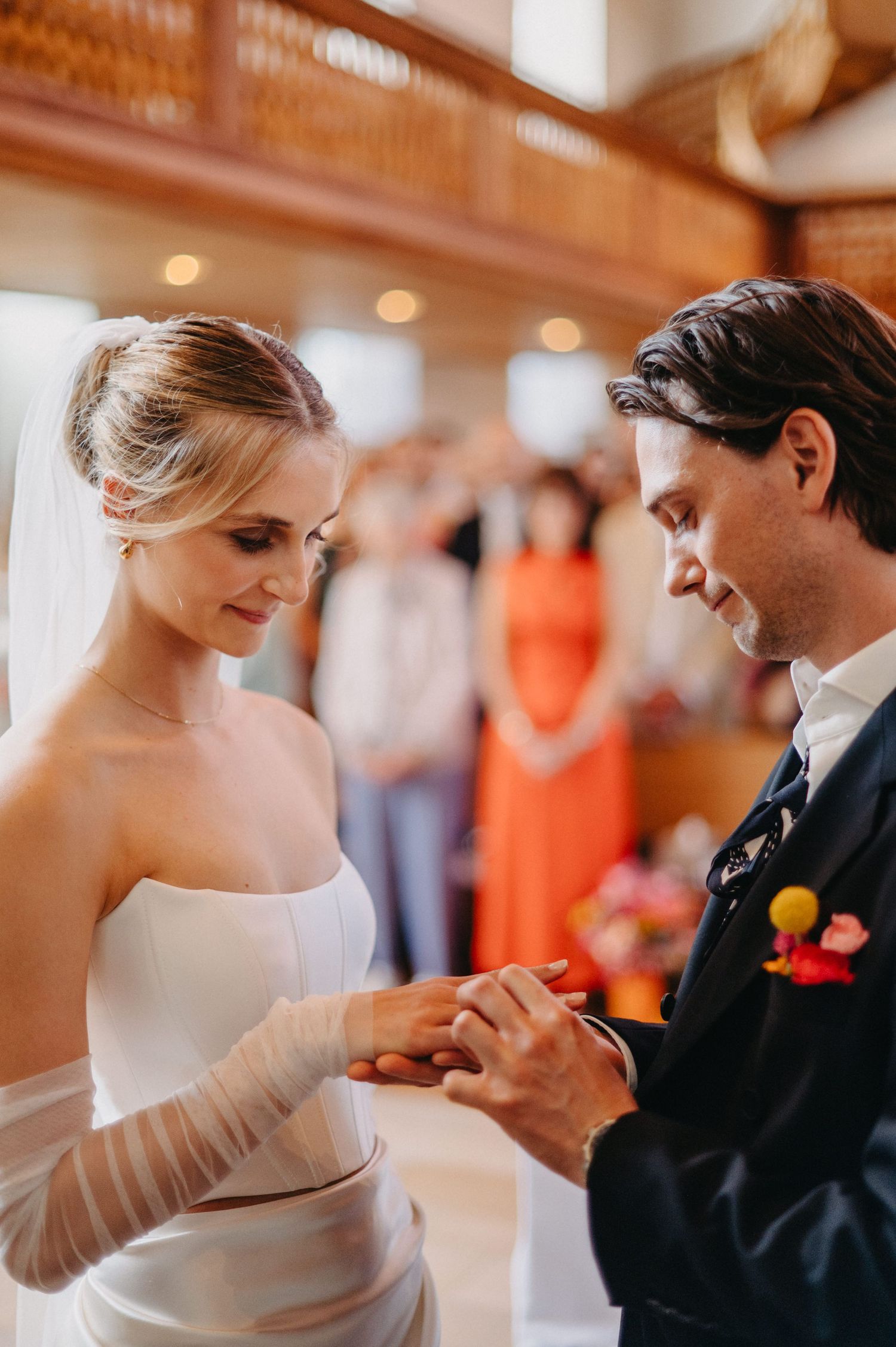 A couple shares an intimate moment during their wedding ceremony as they exchange rings in a warmly lit indoor venue.