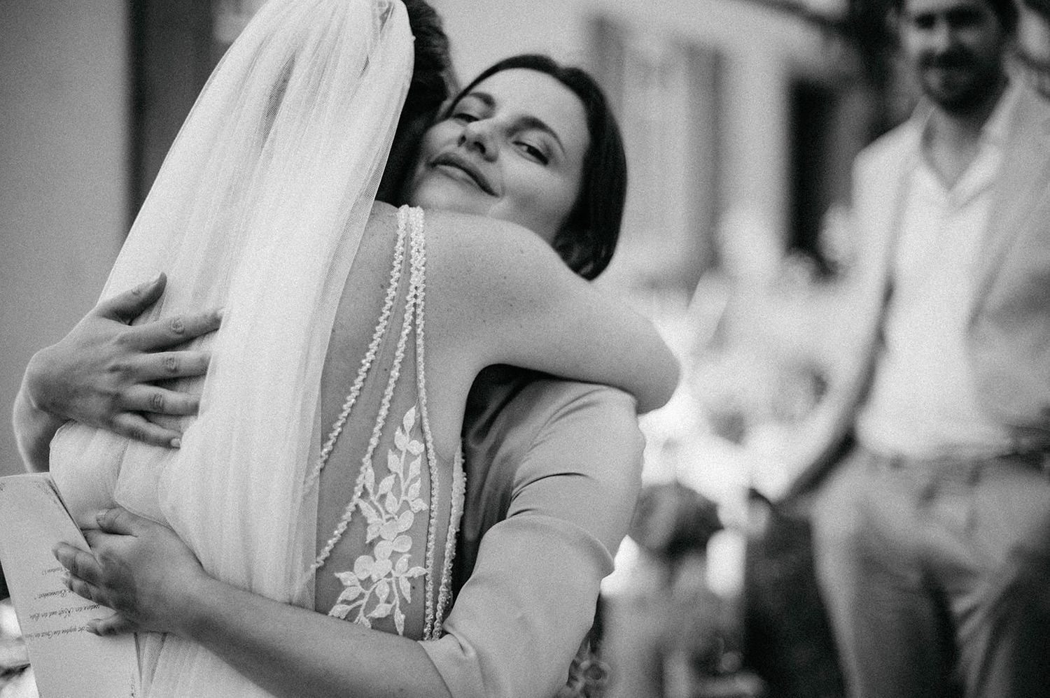 A tender embrace is shared between two people at a wedding celebration, captured in black and white photography.