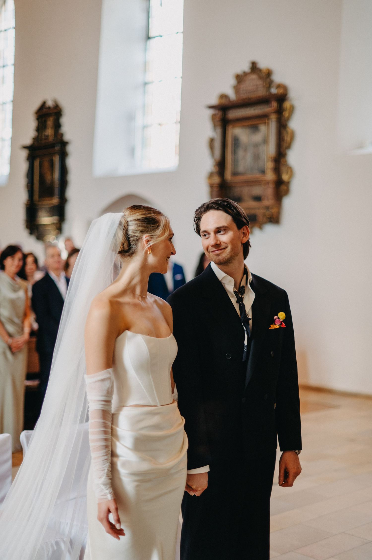 A bride and groom share a joyful moment during their wedding ceremony in a church with ornate frames on the wall.