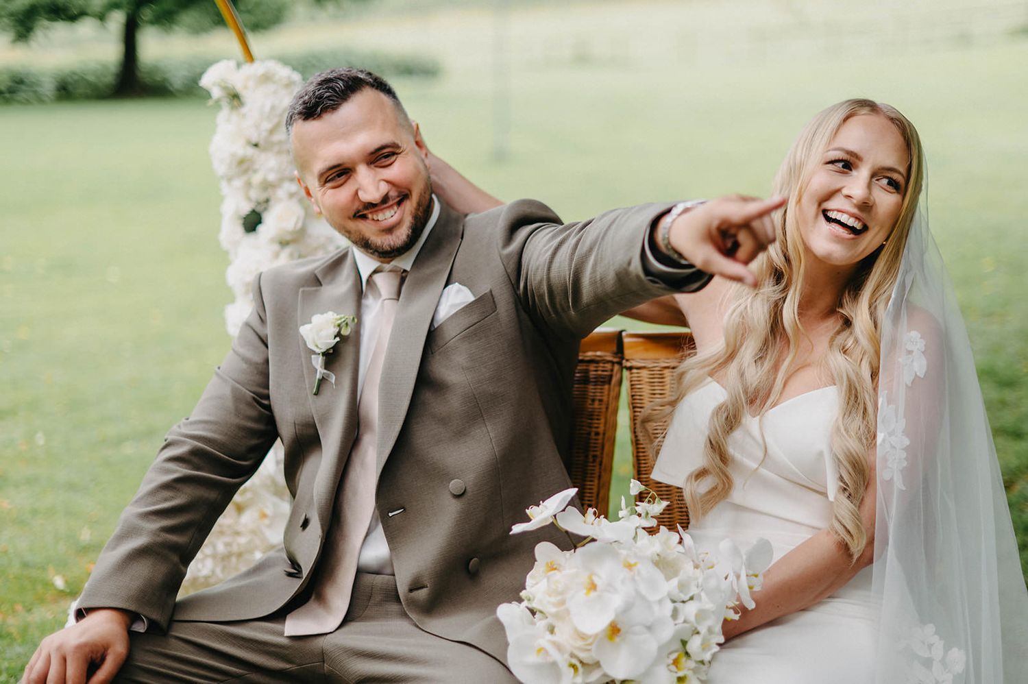 A newlywed couple shares a joyful moment while sitting together outdoors during their wedding celebration.