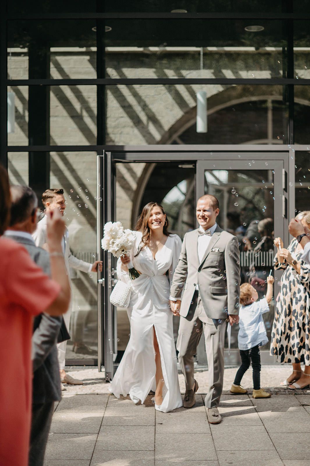 Wedding party celebrating outdoors in front of a building with guests taking photos.