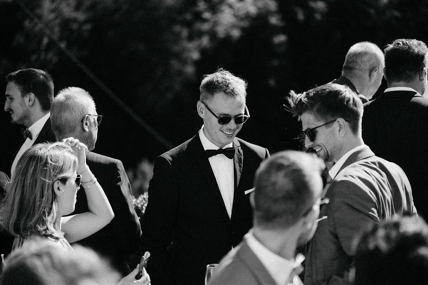 Black and white photo of wedding guests dancing and celebrating at an outdoor reception.