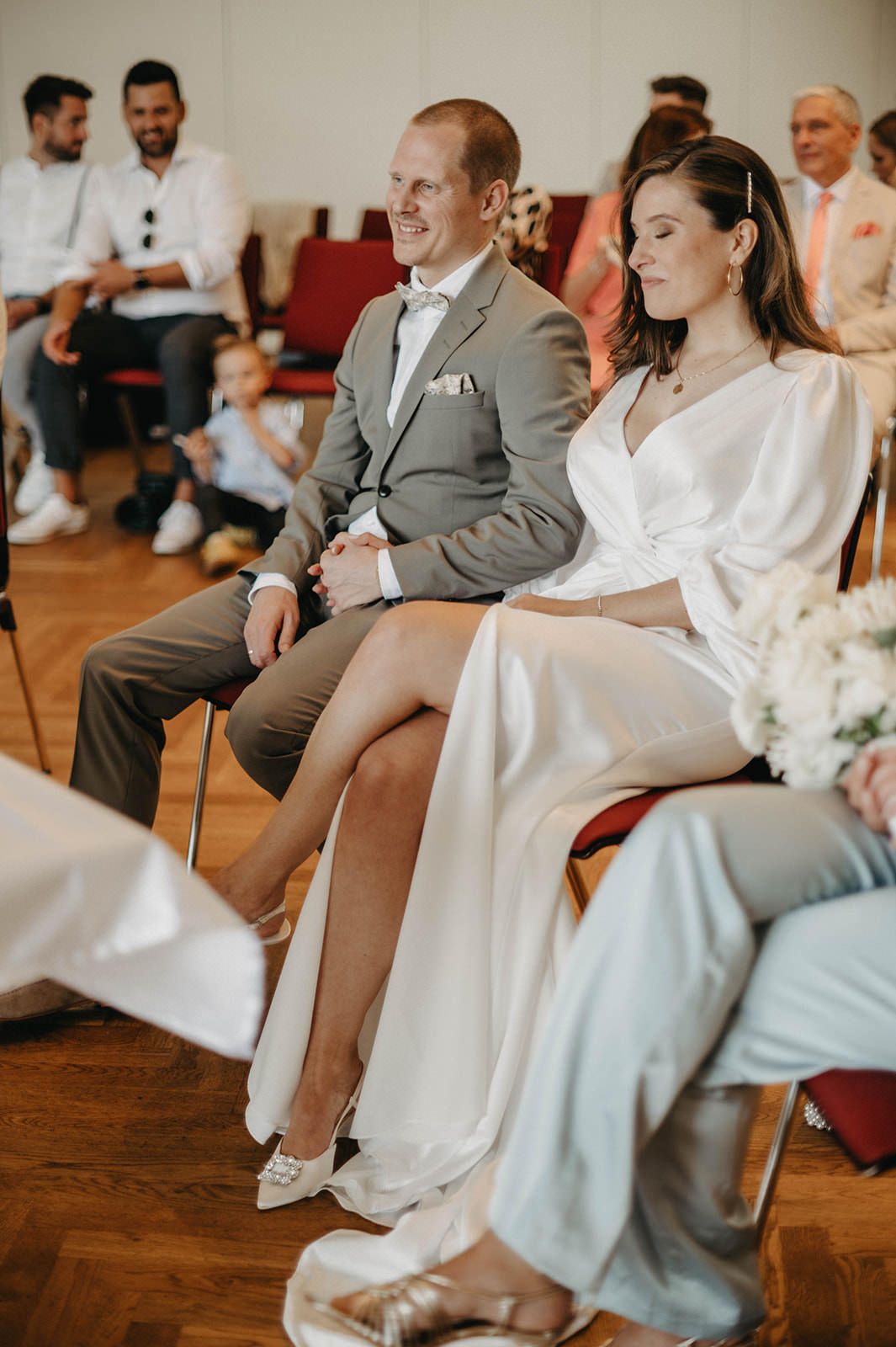 Wedding guests participate in a playful shoe game during the reception seated in wooden chairs on hardwood floors.