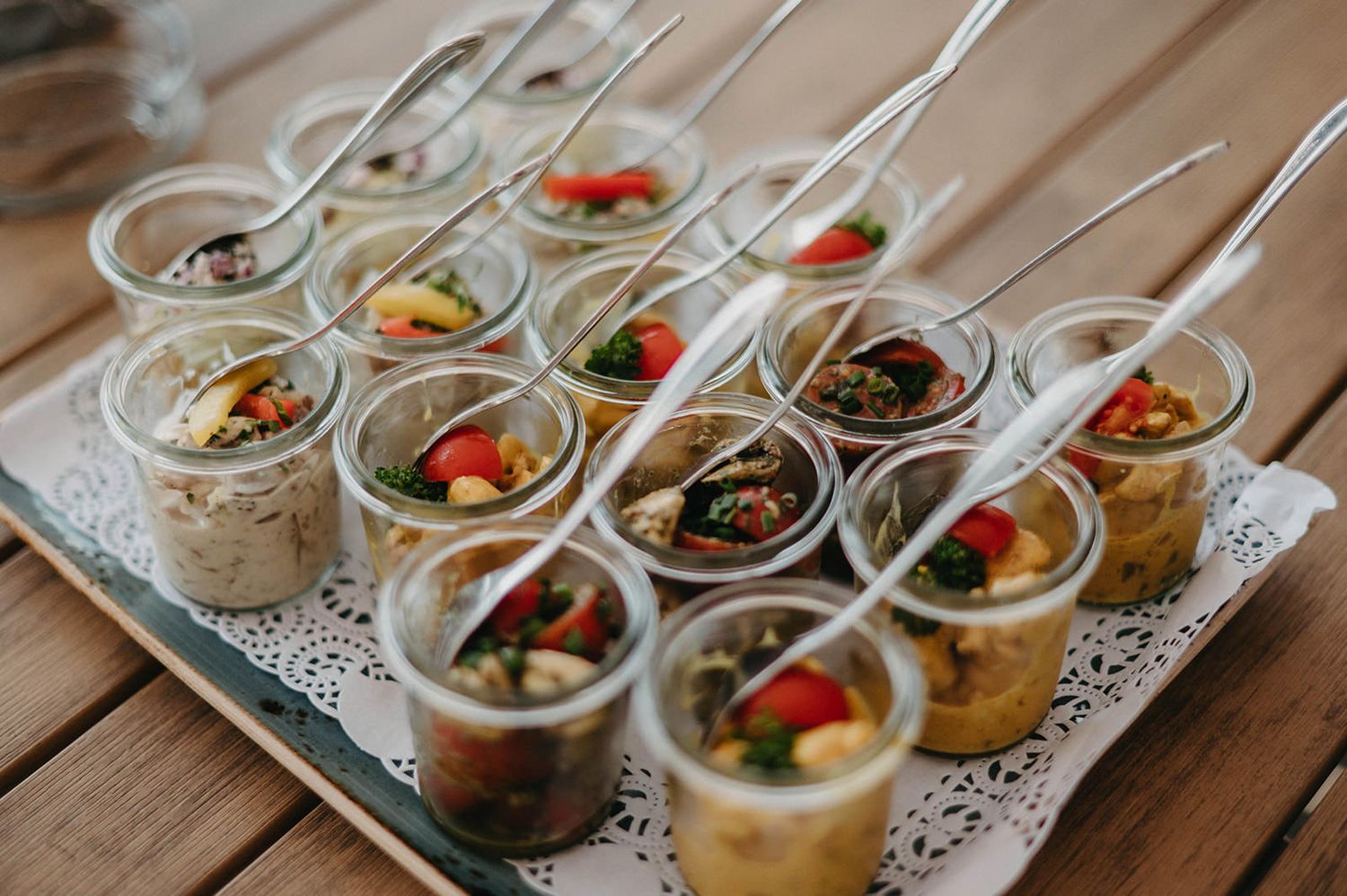 Small glass appetizer cups filled with gourmet bites and garnished with colorful toppings arranged on a serving tray.