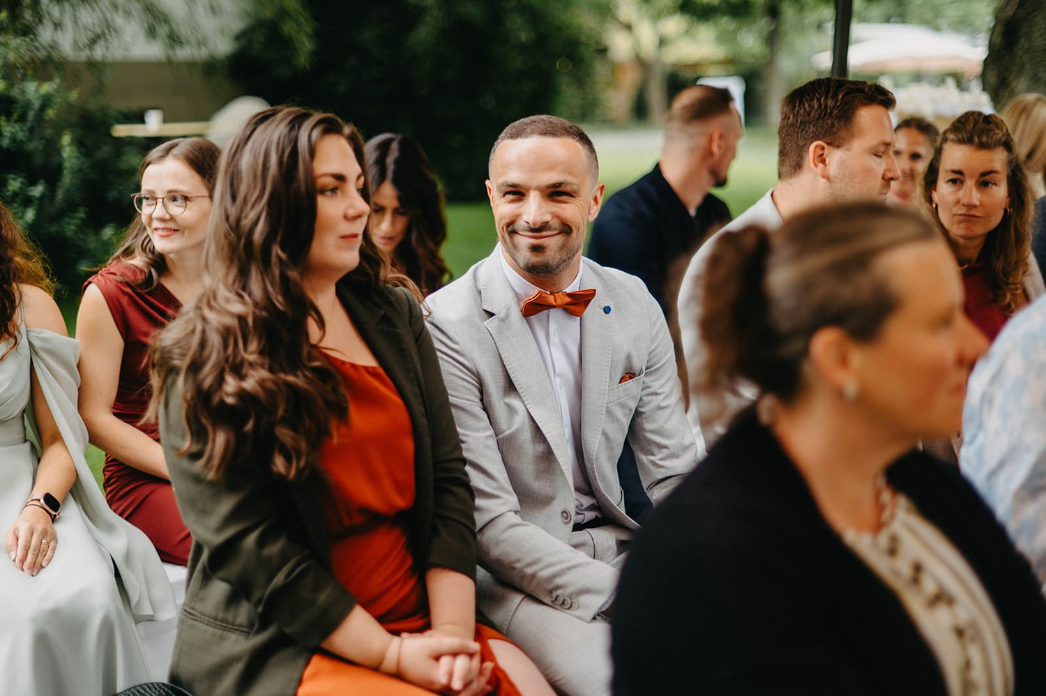 A group of wedding guests laugh and smile together during an outdoor celebration.