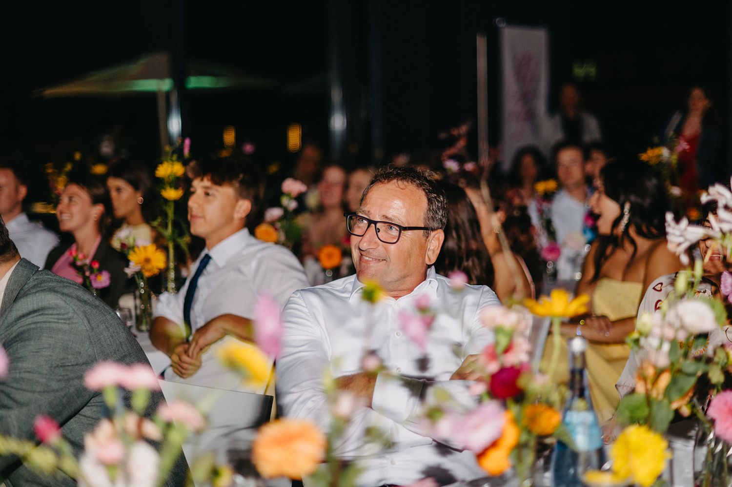 A festive banquet hall decorated with colorful flowers and filled with guests seated at round tables for a celebration.
