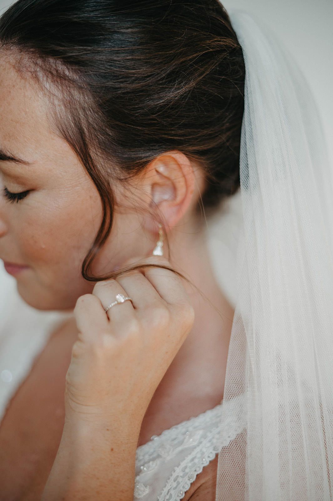 Close-up side profile of a bride wearing pearl earrings and delicate lace veil against light background.