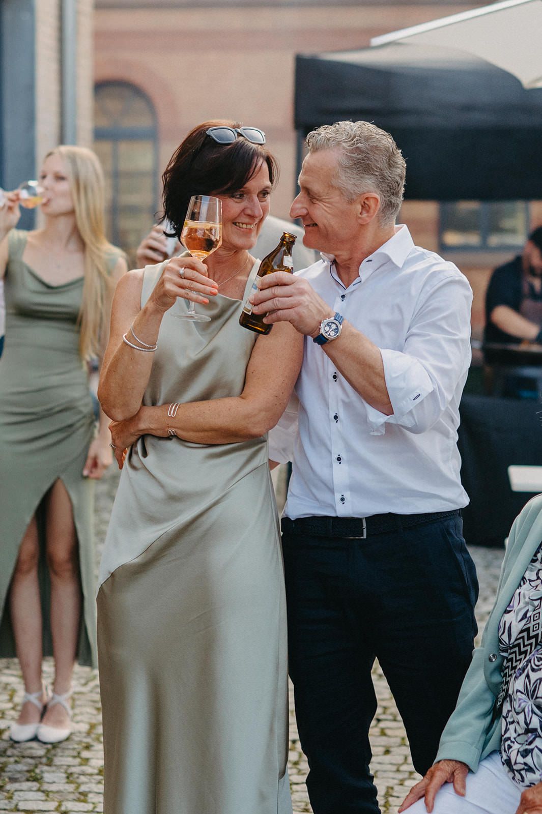 A couple dances together at an outdoor event while holding wine glasses and sharing a romantic moment.