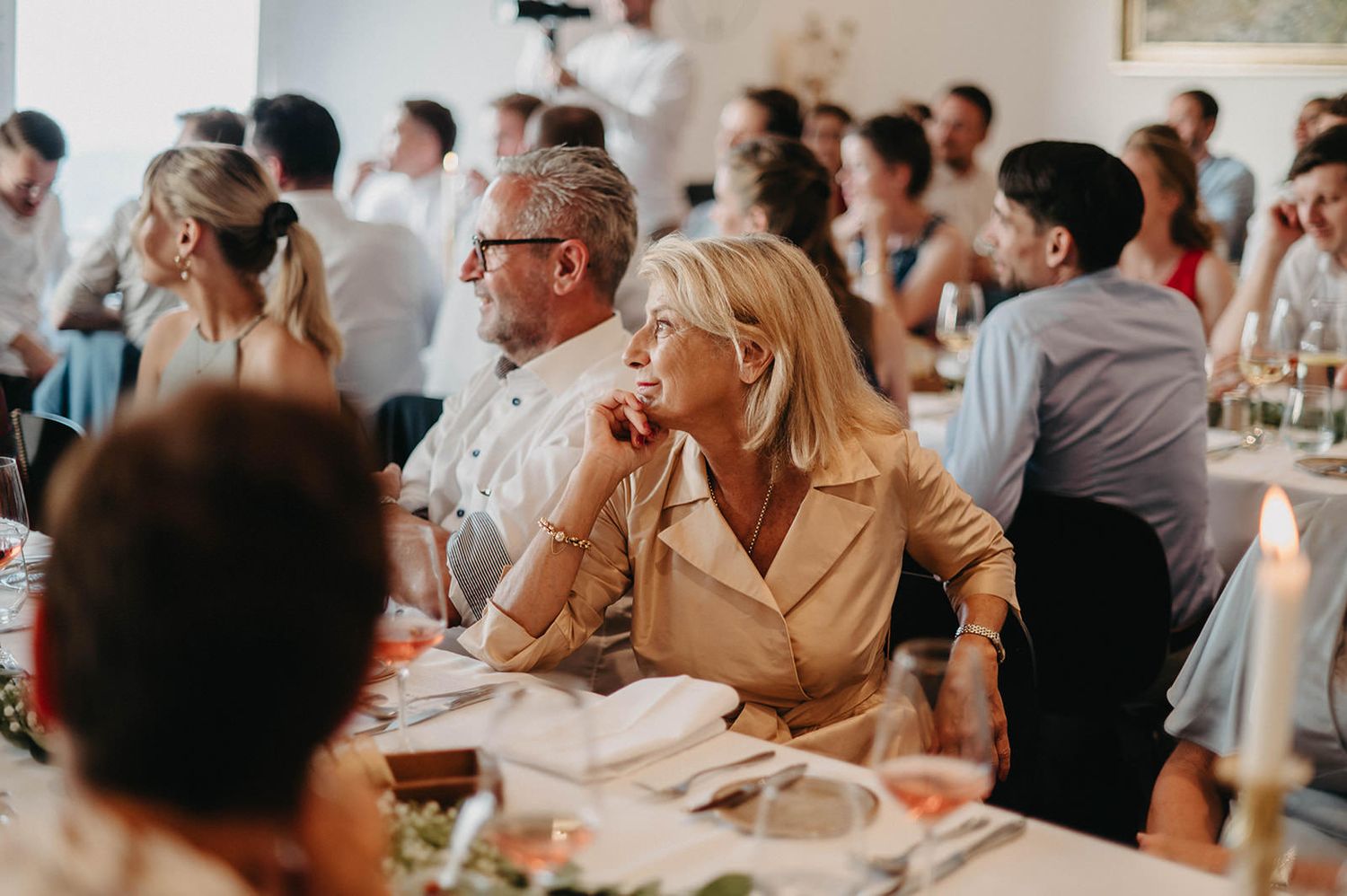 Wedding guests enjoy a candlelit dinner reception at elegantly decorated tables in a bright, airy venue.