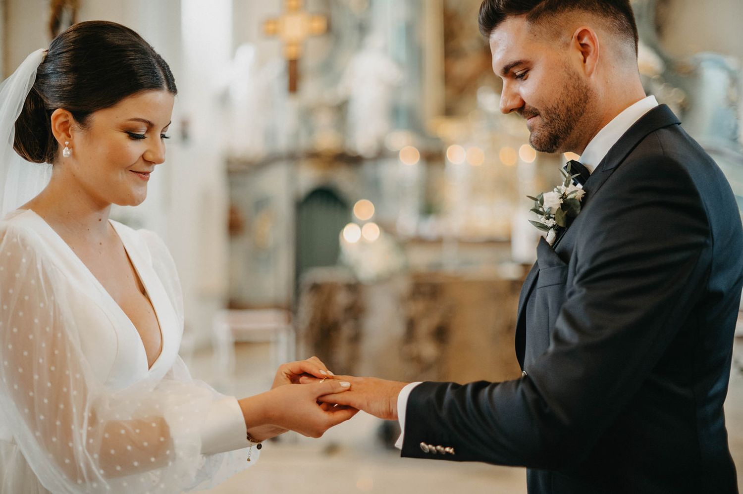 A bride and groom exchange rings during an intimate wedding ceremony in a warmly lit indoor venue.
