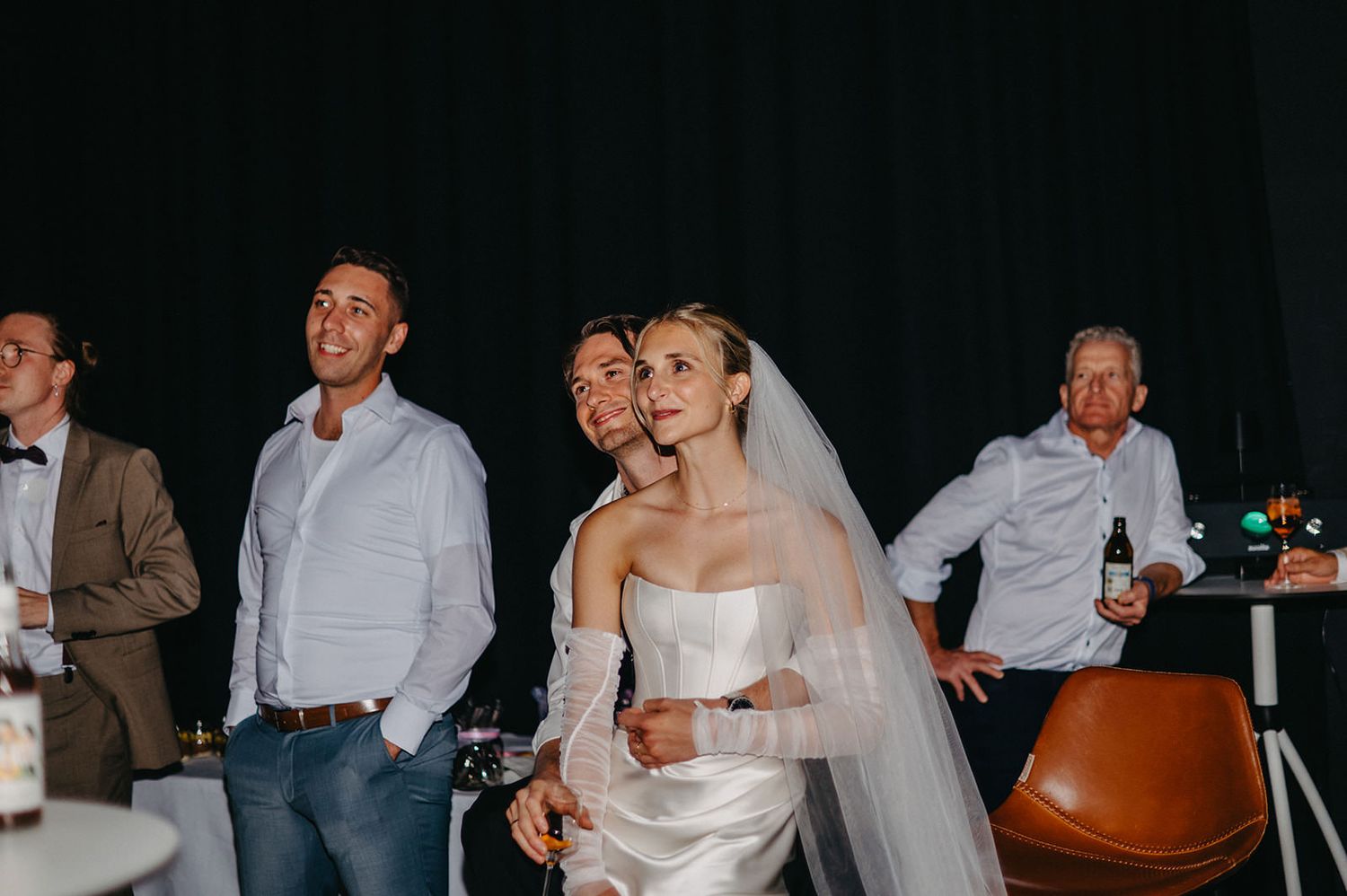 Wedding guests enjoy candid moments during a reception celebration in a dark venue with ambient lighting.