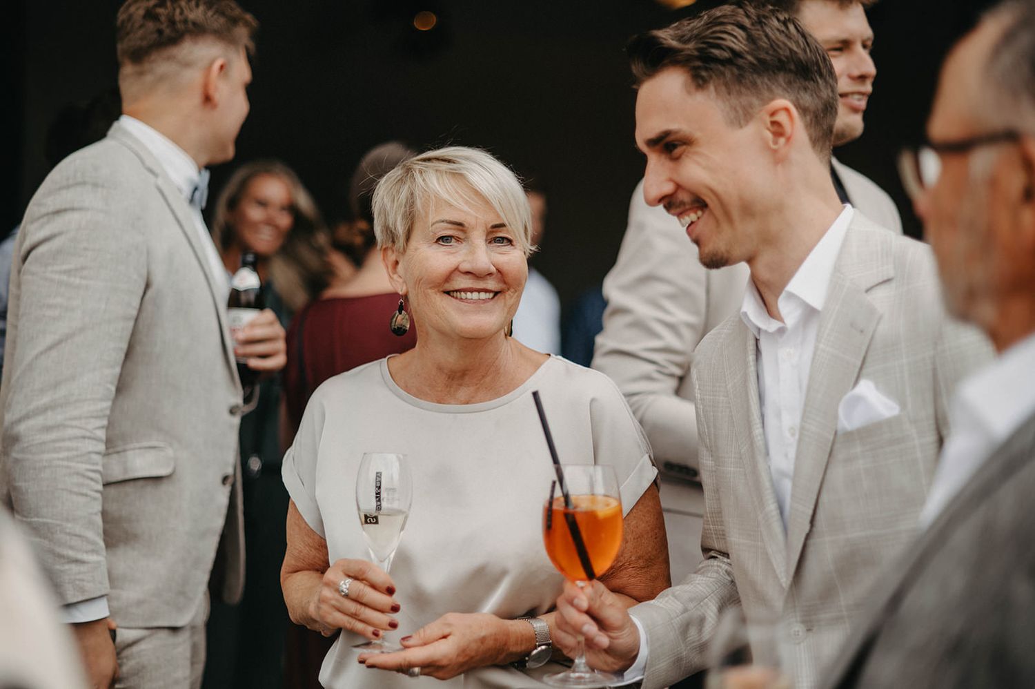 Wedding guests in light colored attire gather outdoors for a celebratory moment during a reception.