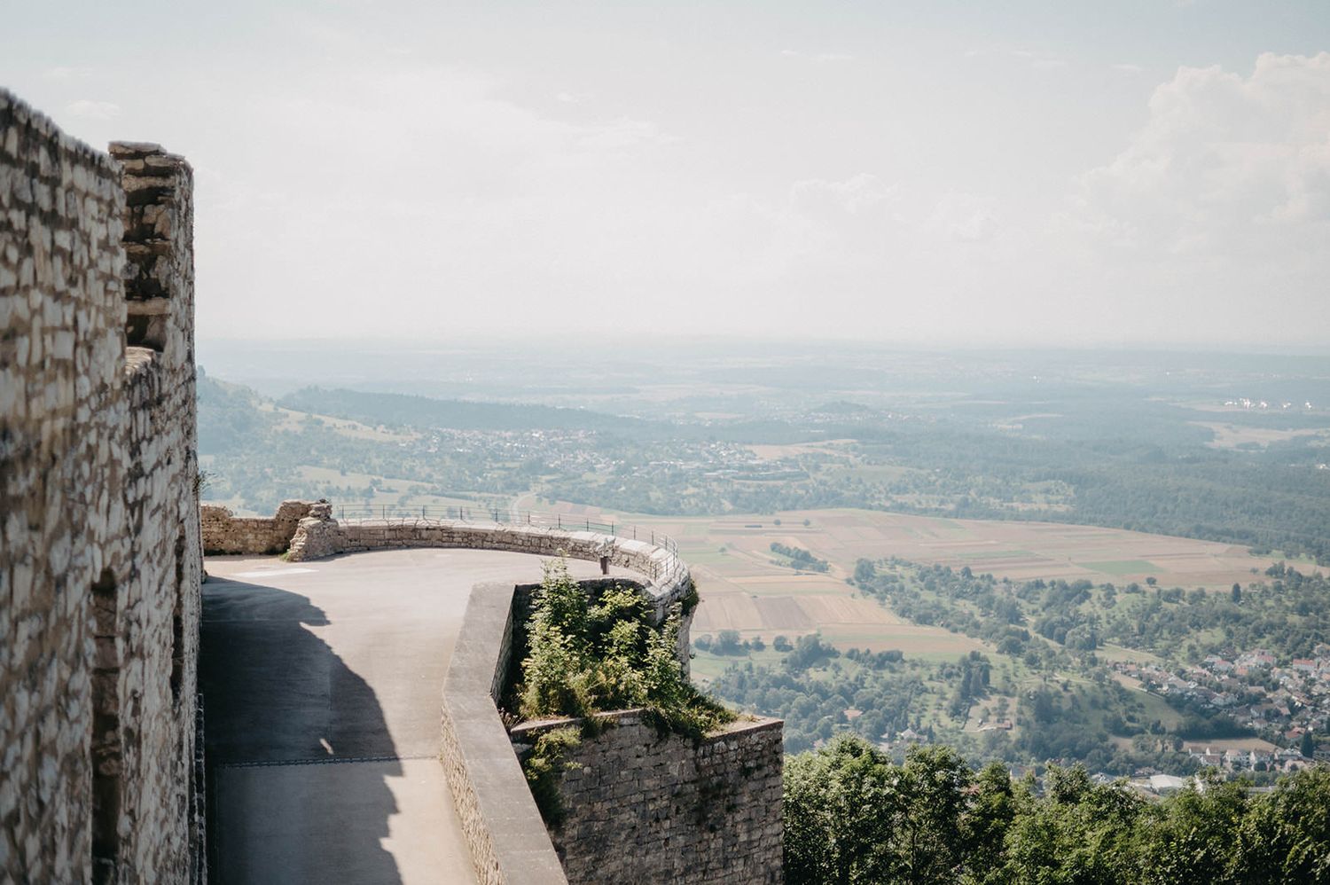 Ancient stone castle walls and lookout points offer panoramic views over a scenic European countryside landscape.