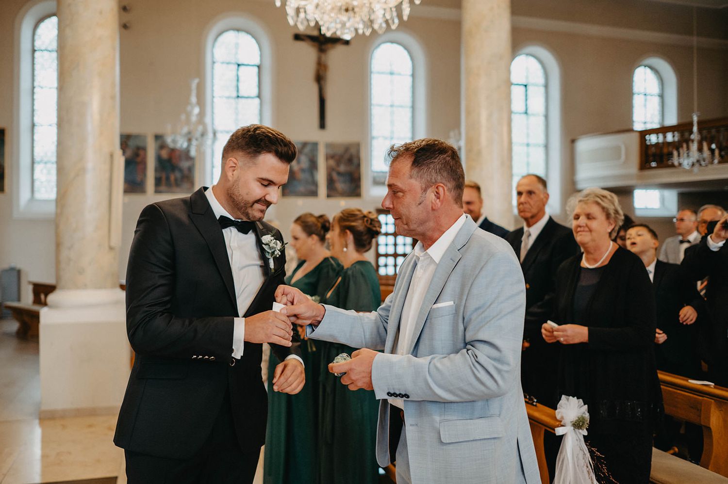 Wedding ceremony in a bright church interior with guests watching as two people exchange rings.