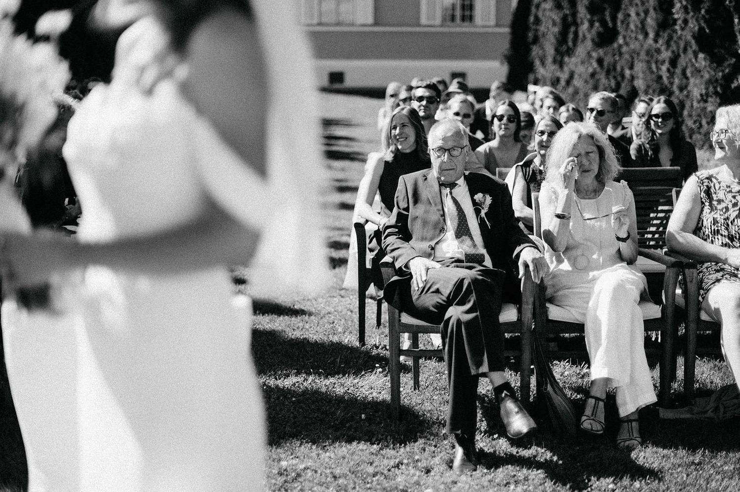 Black and white photo series showing wedding guests mingling on a grassy lawn during an outdoor celebration.