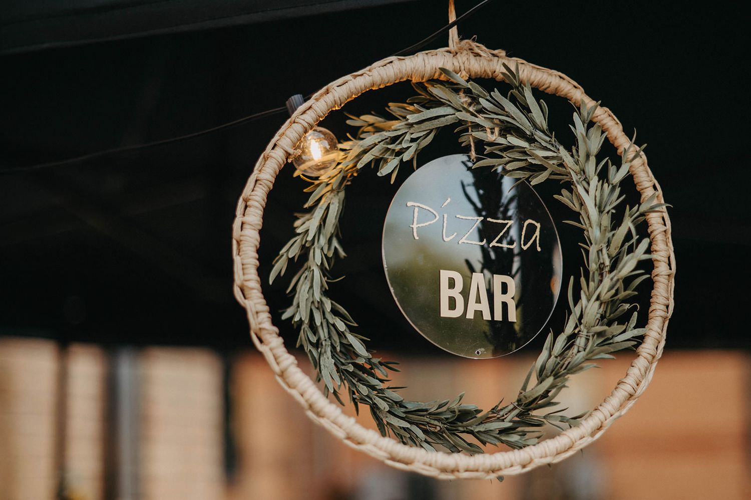 Rustic wedding decor featuring circular glass signs with greenery wreaths and text displayed at a reception bar.