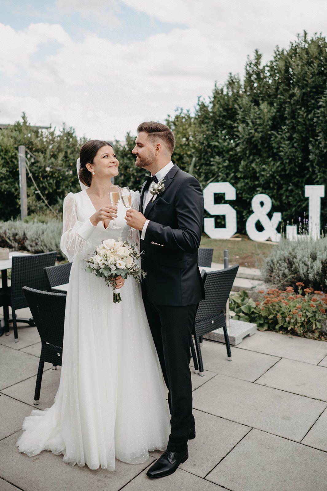 A couple shares a romantic moment during their wedding photoshoot on a patio with greenery in the background.