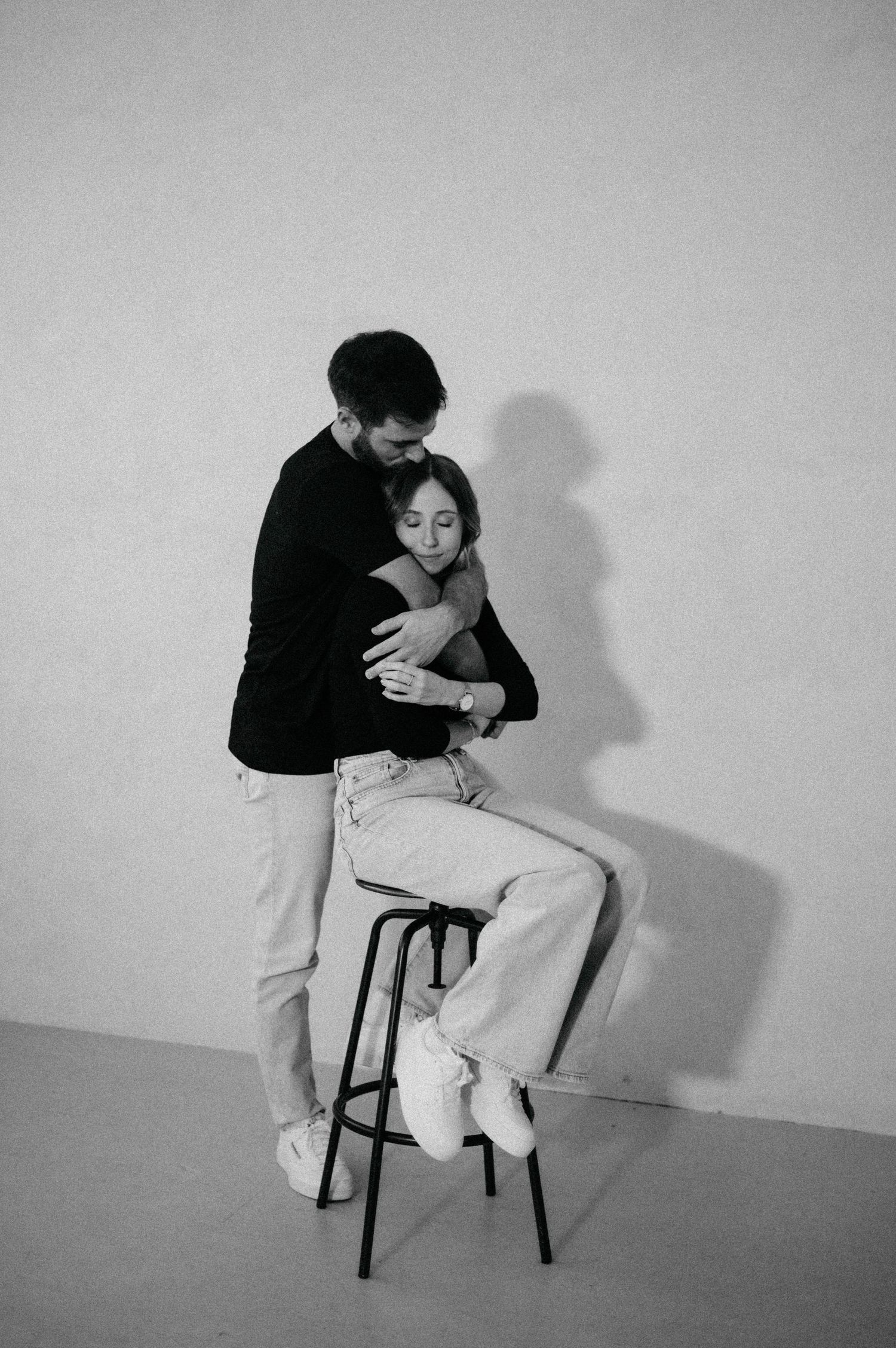 A minimalist black and white portrait showing an intimate embrace on a bar stool.