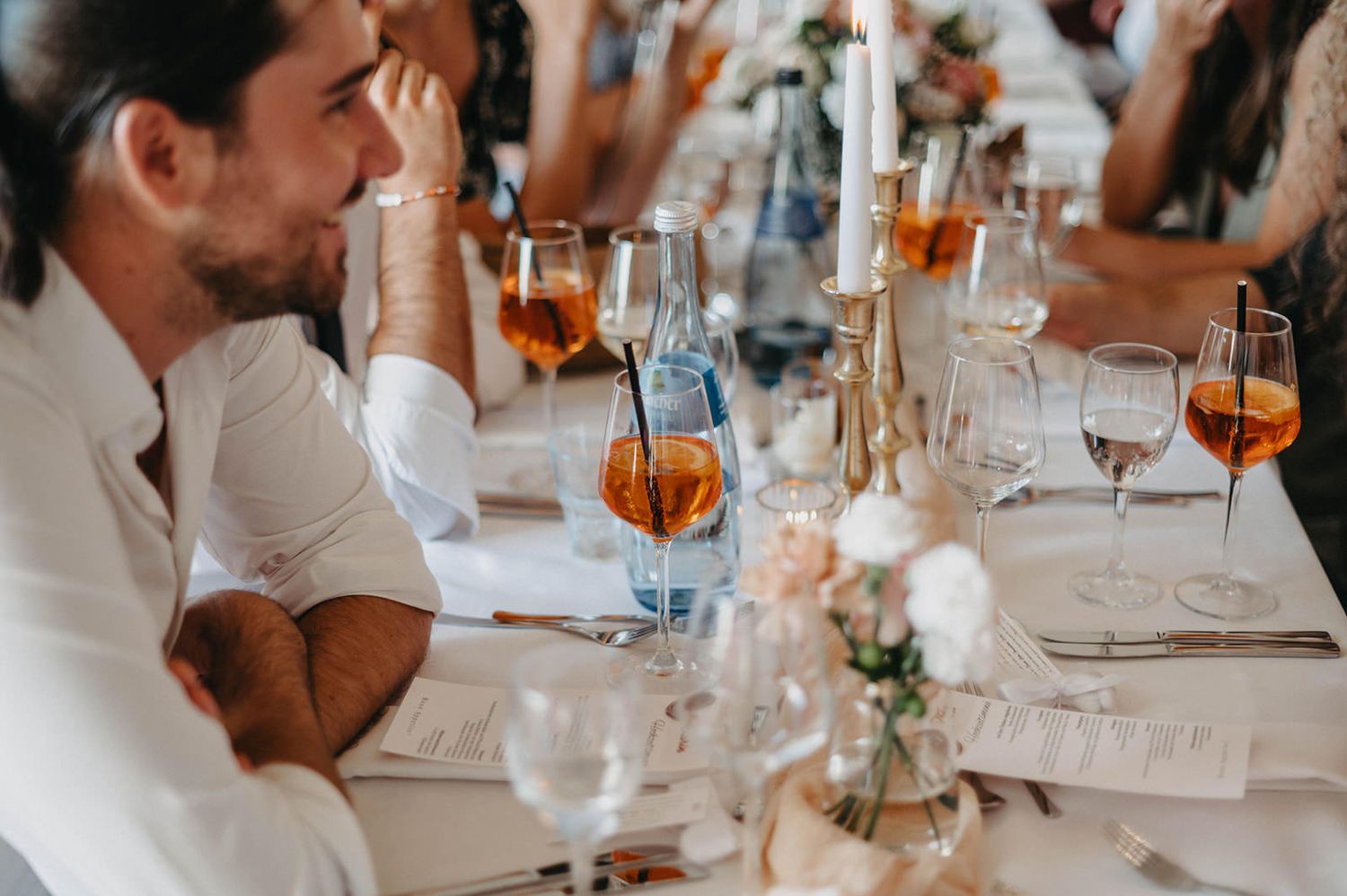 A group of people enjoying drinks and conversation at an elegant restaurant table with wine glasses and place settings.