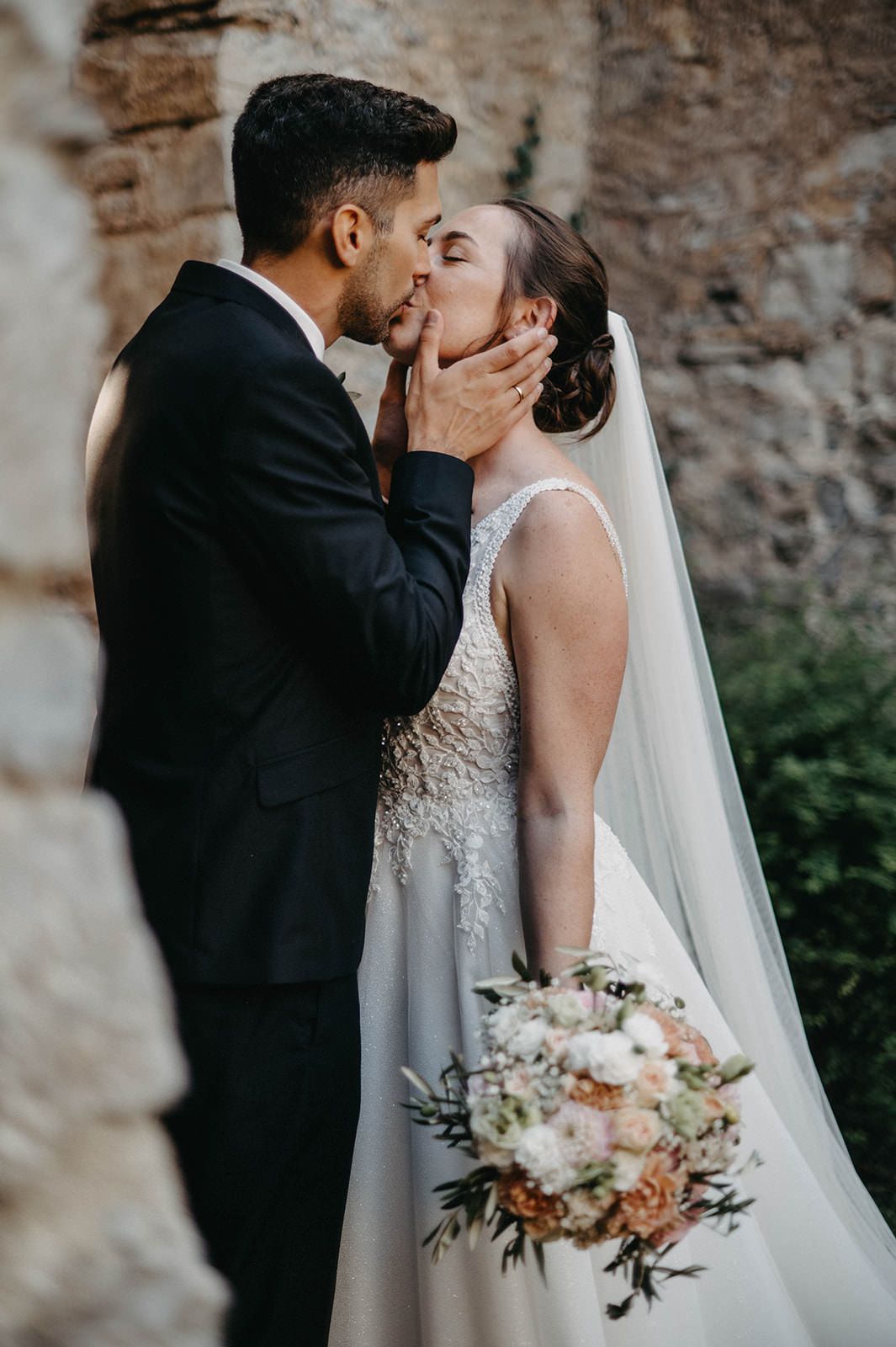 A romantic wedding moment captured against a stone wall as the bride holds a beautiful blush and white bouquet.