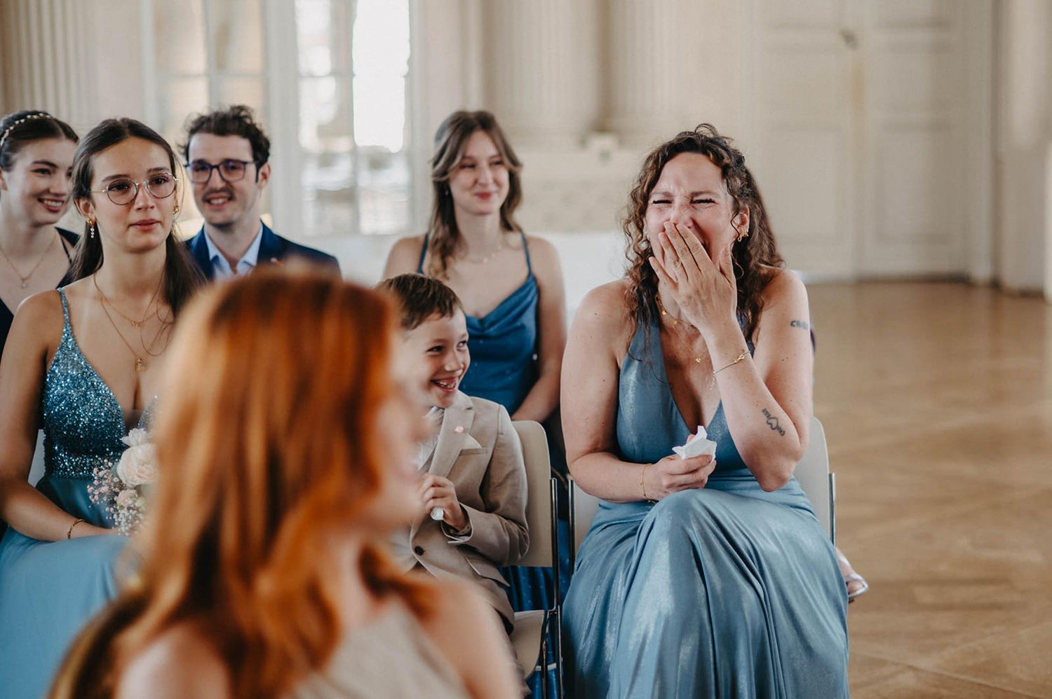 Bridesmaids in elegant blue dresses share emotional reactions during a wedding ceremony.