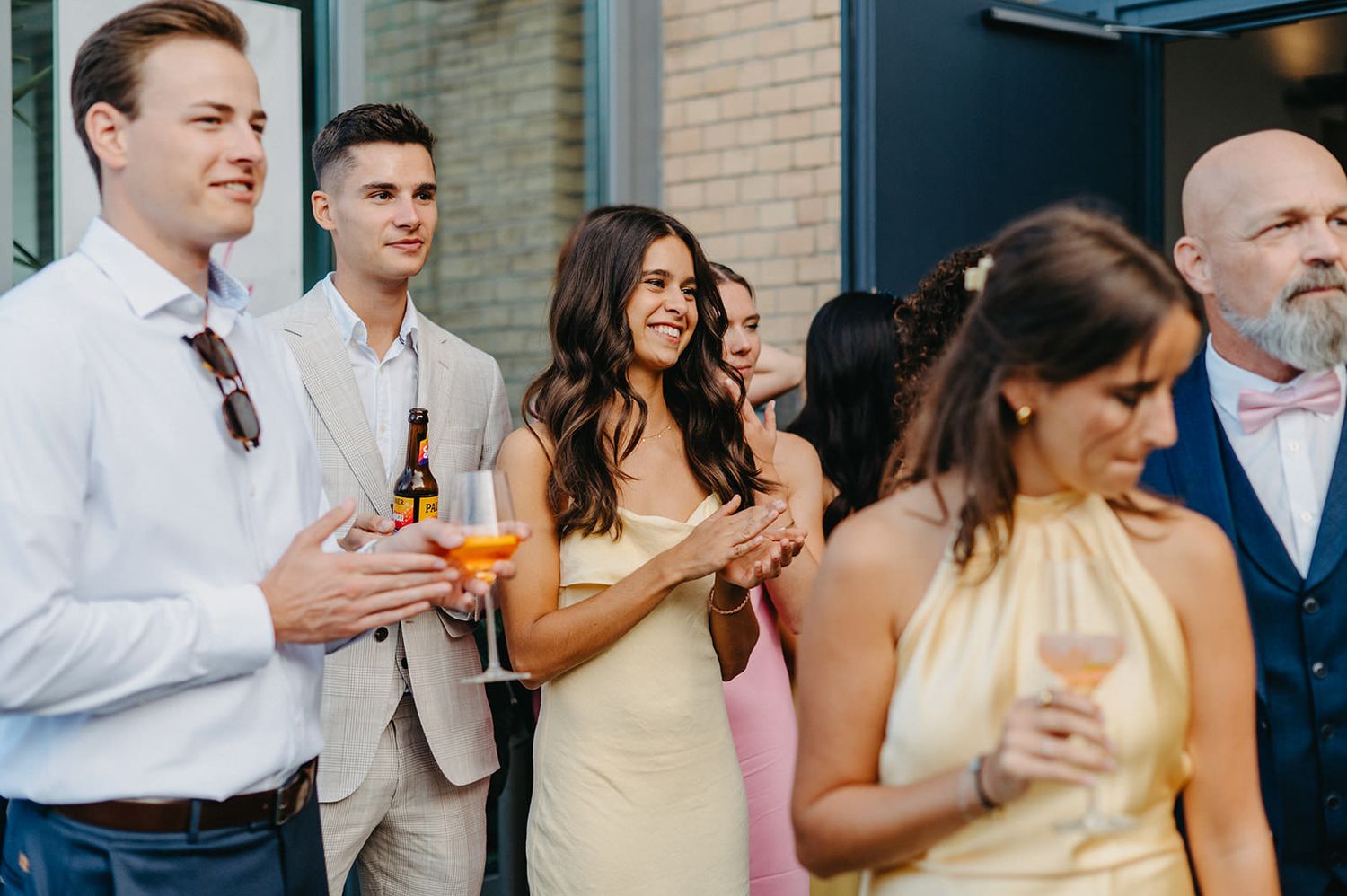 Wedding guests in pastel attire socialize and enjoy drinks during an outdoor cocktail reception.
