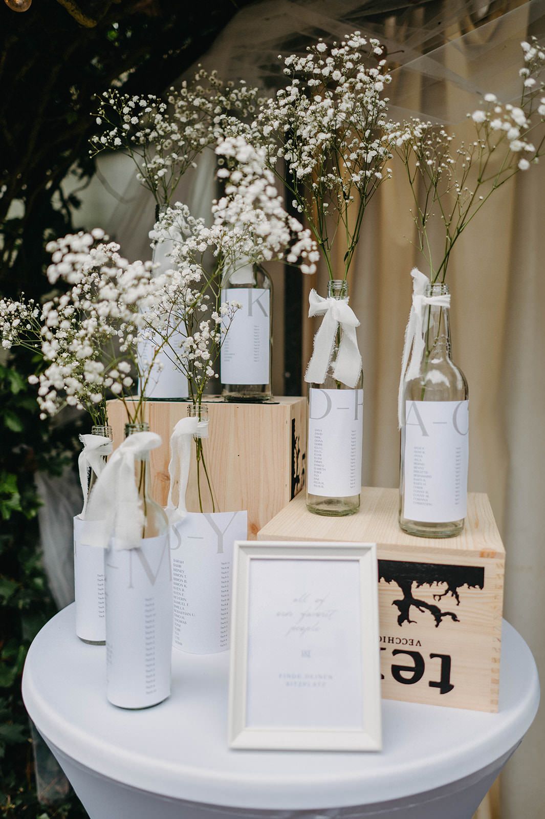 White glass vases with baby's breath flowers and paper tags arranged on a round white table create an elegant display.