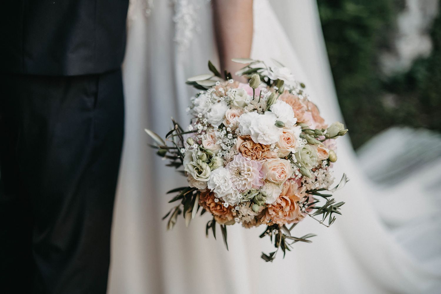 A delicate bridal bouquet featuring blush pink roses, white flowers and greenery against a soft neutral background.