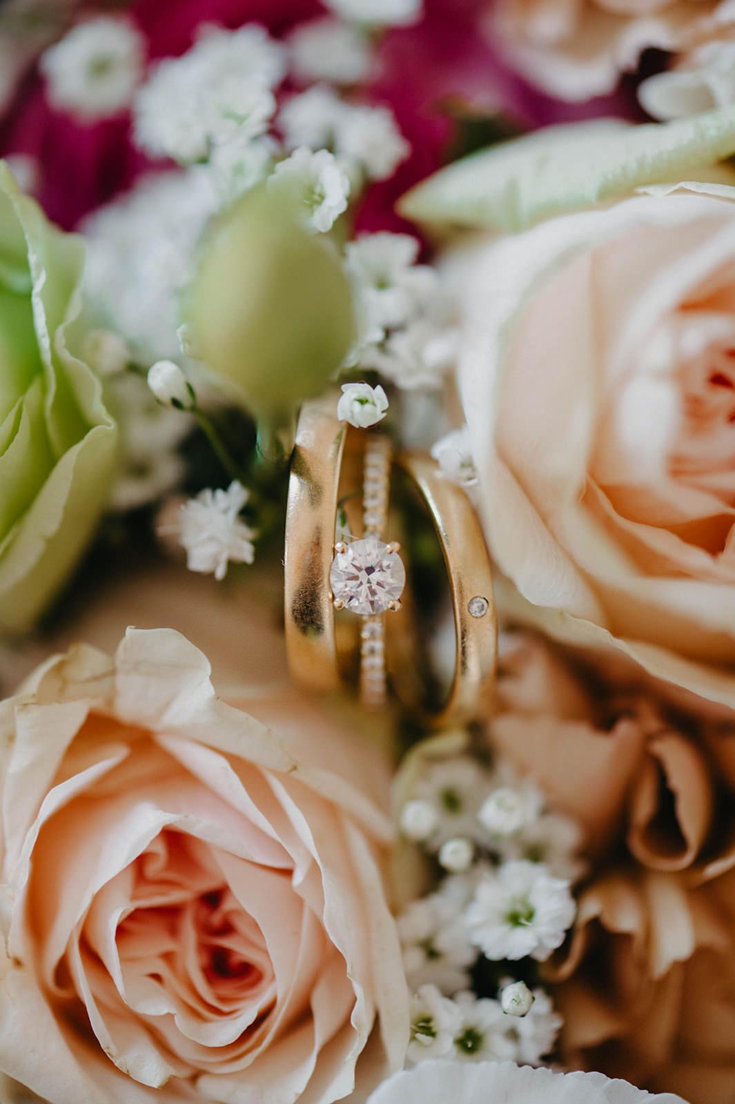 Close-up detail of peach roses and wedding rings with delicate baby's breath flowers in a romantic arrangement.