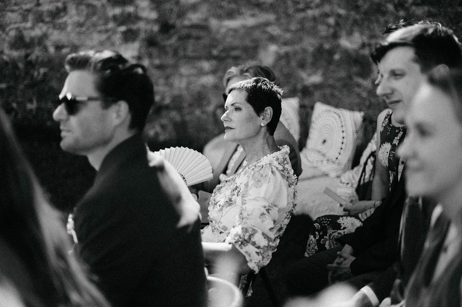 A vintage black and white photograph showing people seated outdoors, with one person wearing sunglasses.