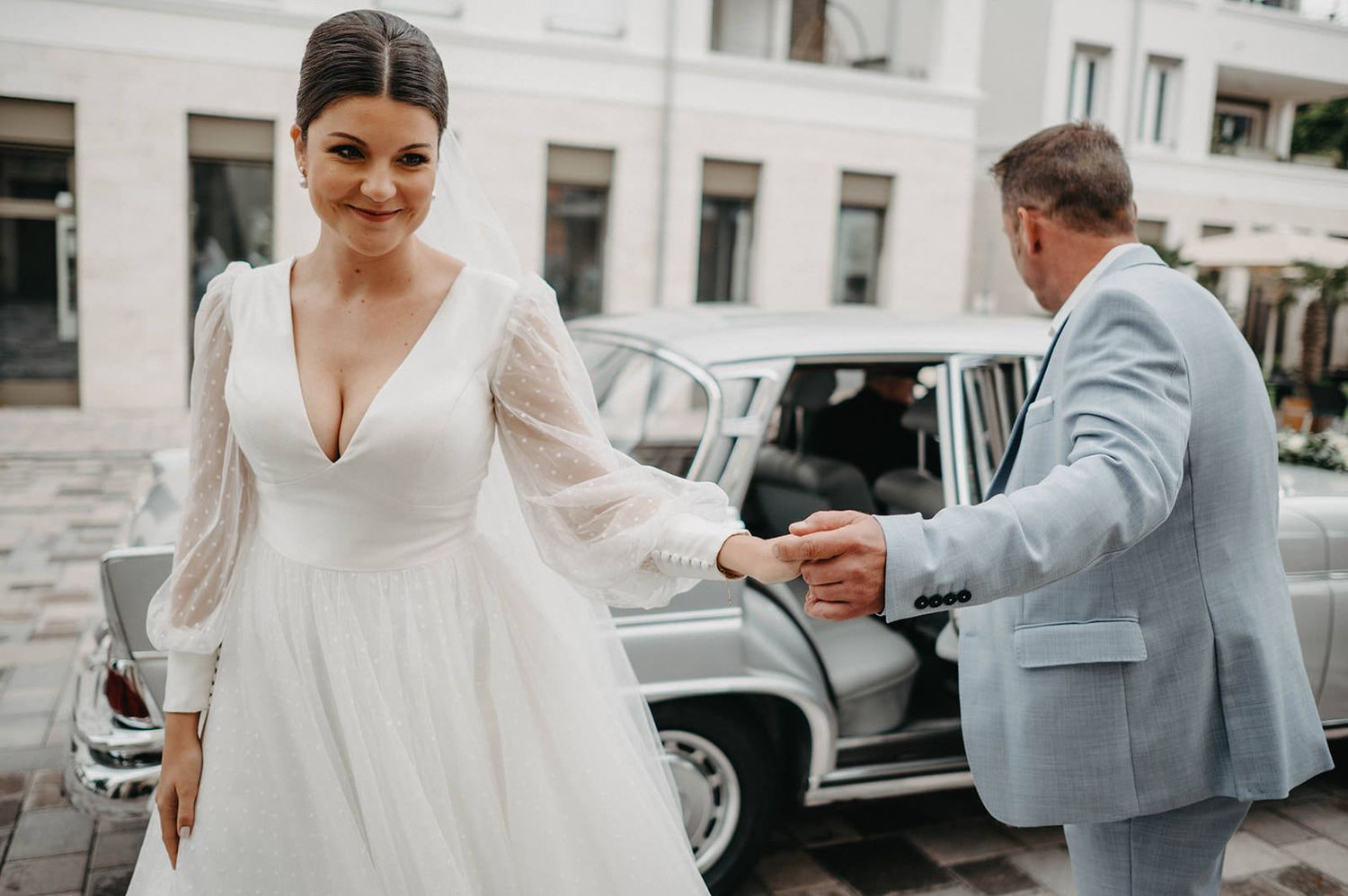 A bride and groom stand together near a classic vintage car during their wedding photo session.