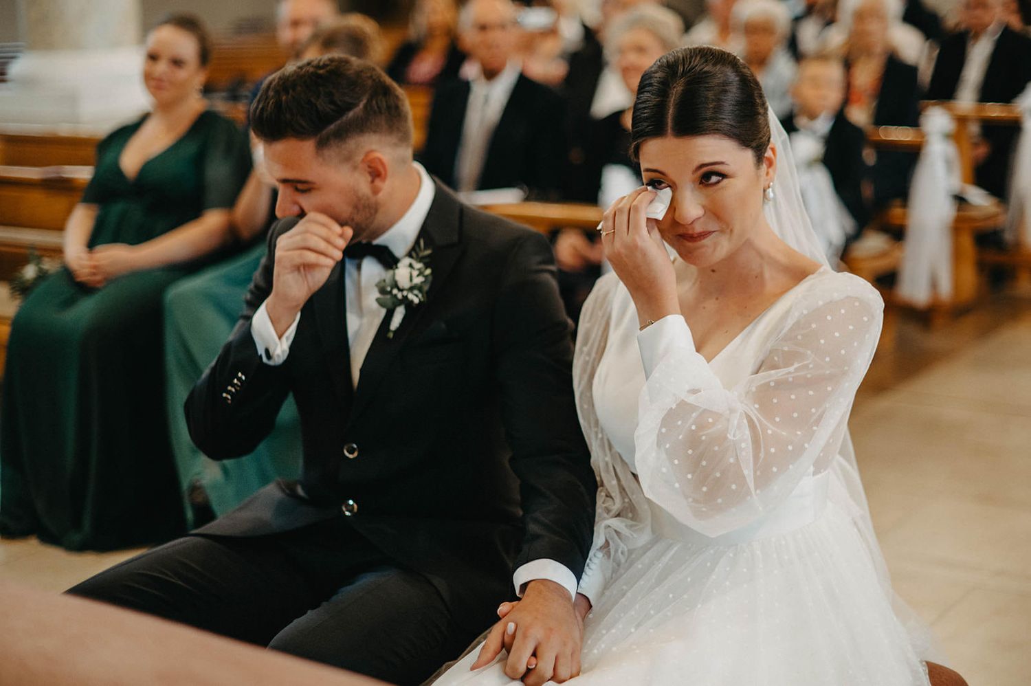Bride and groom share emotional reactions during wedding ceremony in wooden church interior.