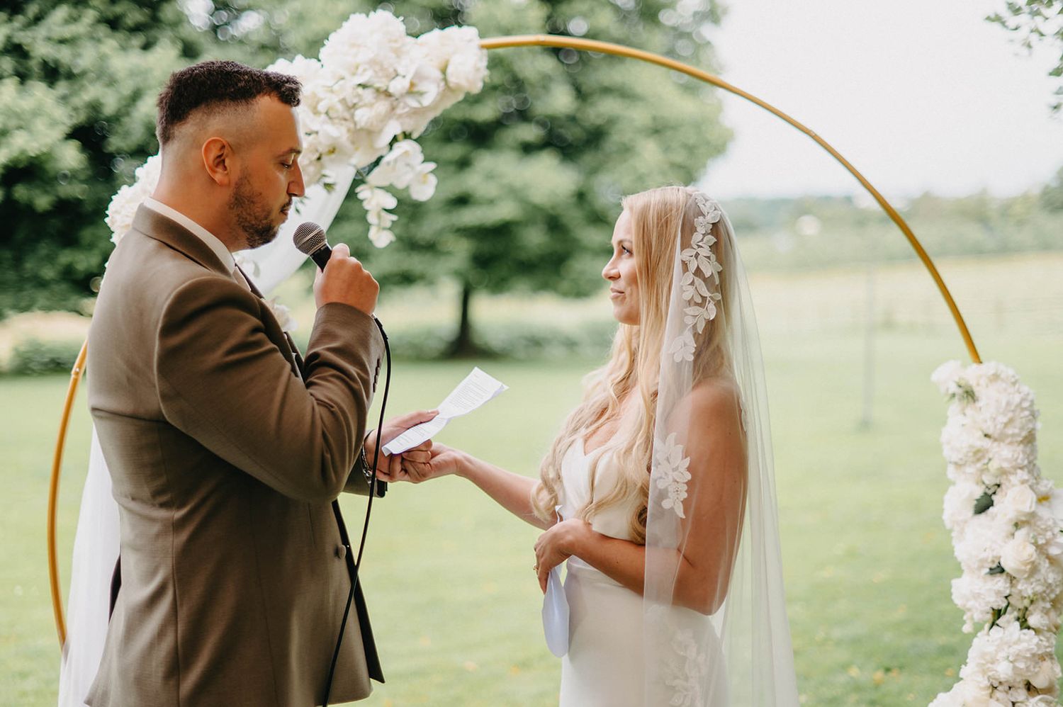 Newlywed couple shares intimate moments during outdoor wedding ceremony in a lush green garden setting.