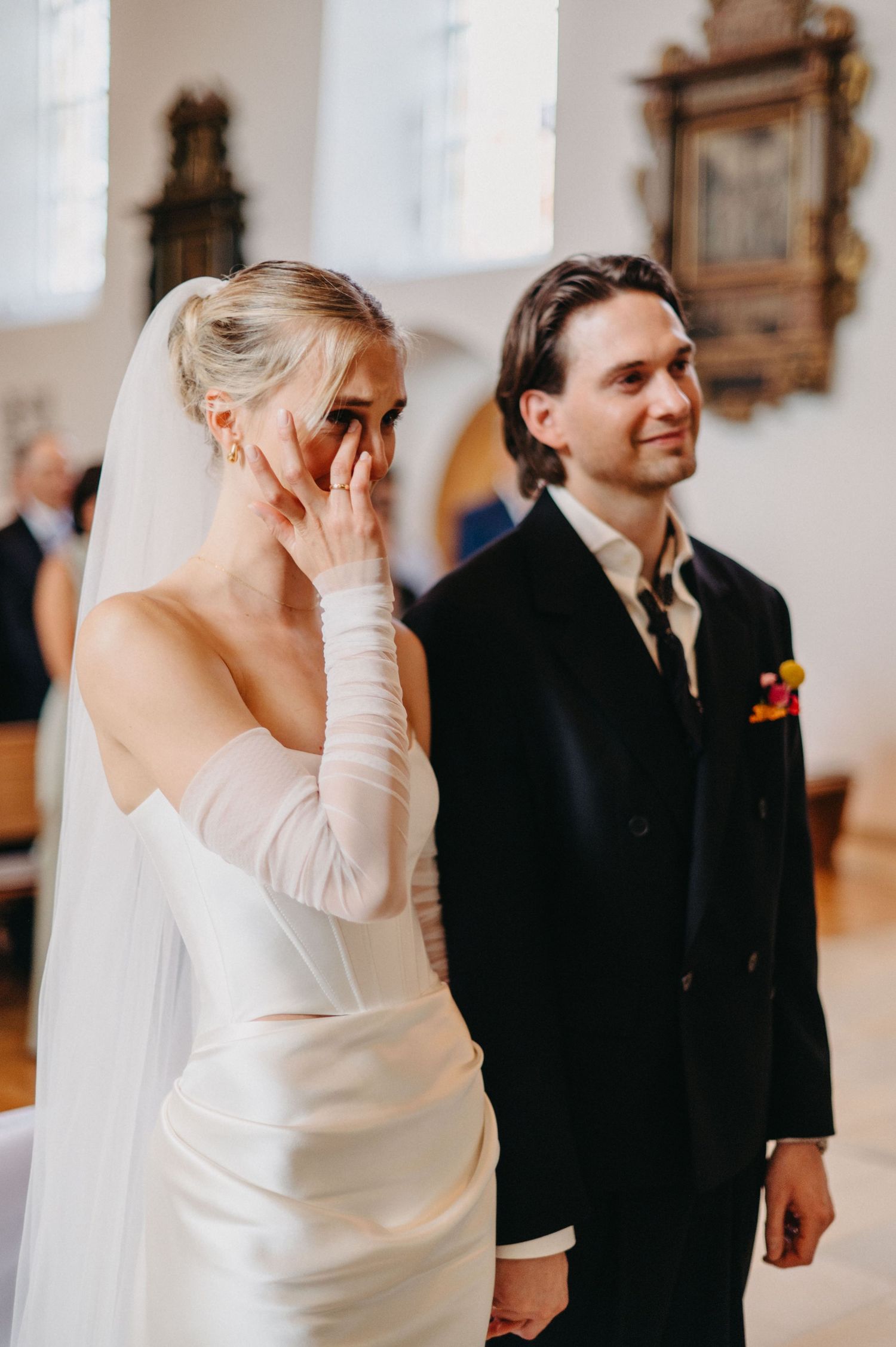 A bride and groom share a tender moment during their wedding ceremony in a bright, elegant church setting.
