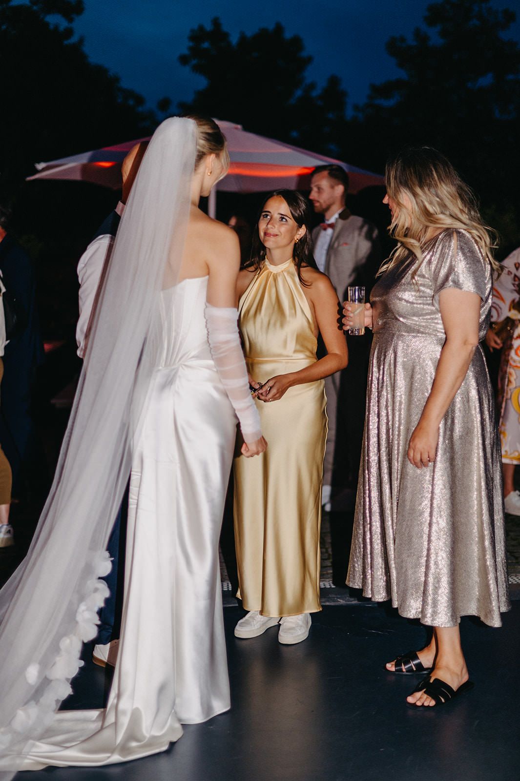 Wedding guests in evening attire gather on a dark dance floor with a bride in a flowing white gown and veil.