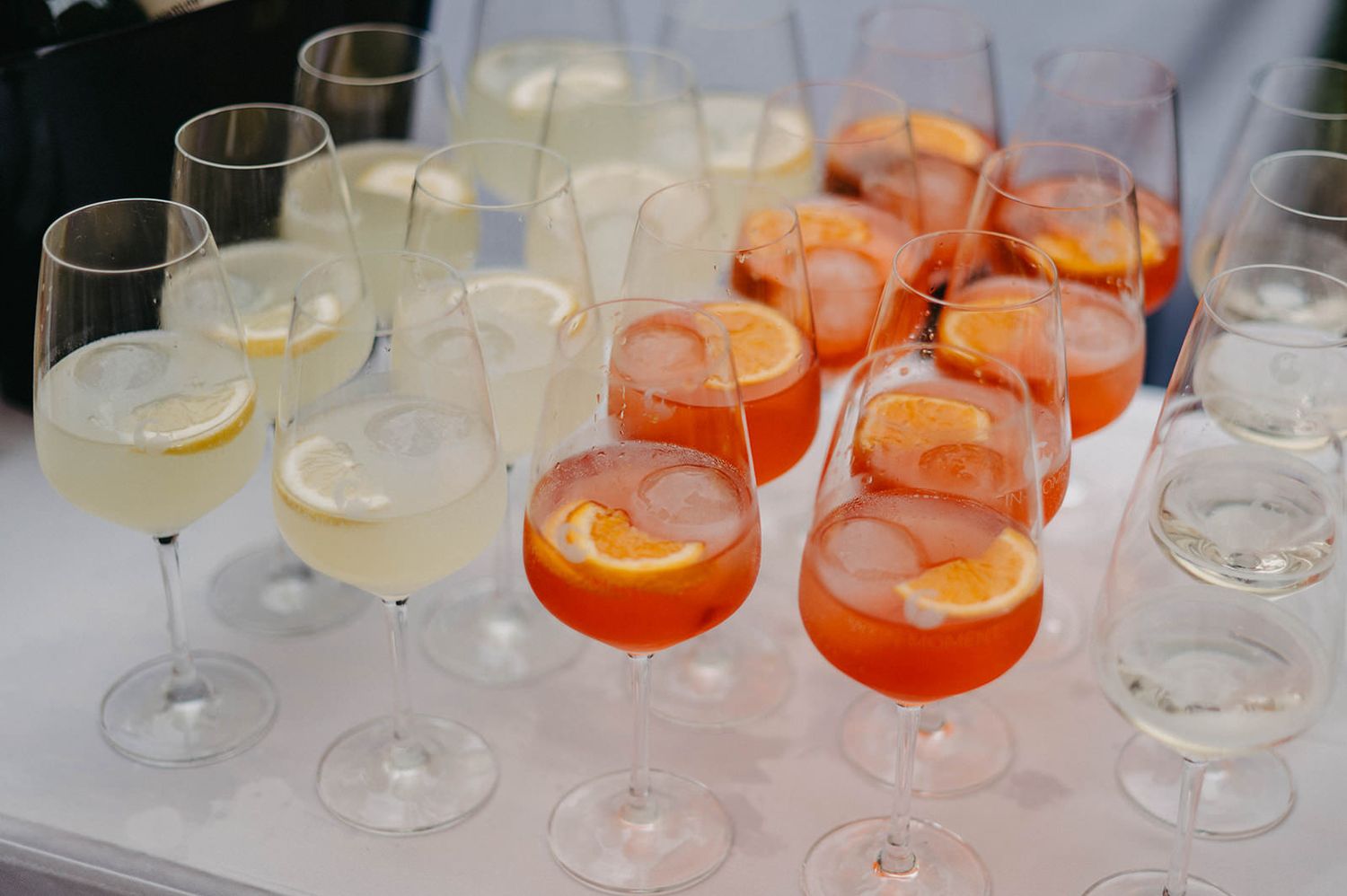 Row of elegant cocktail glasses filled with various colorful drinks on a white surface.