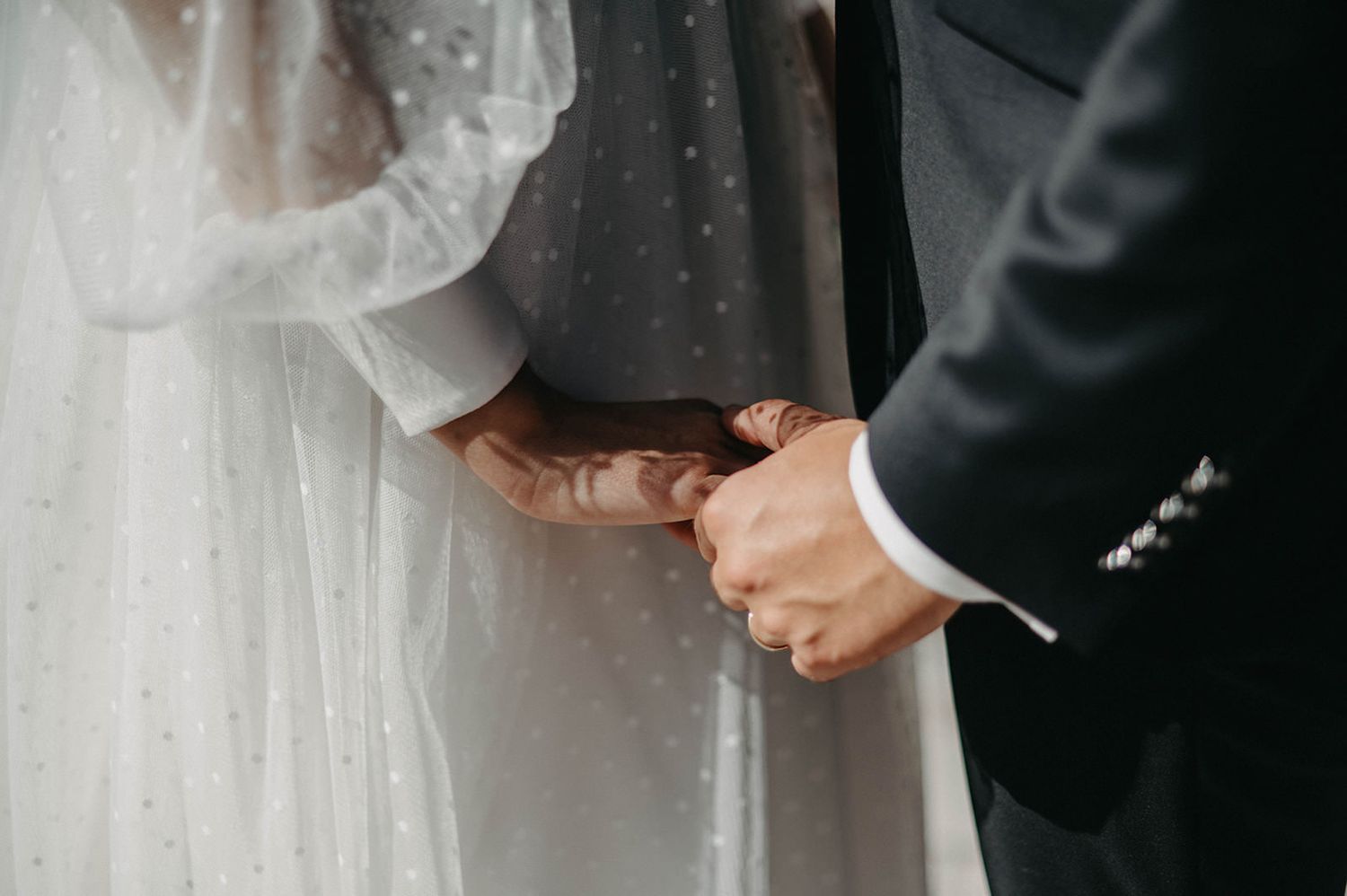 Close-up detail of a bride and groom holding hands during their wedding ceremony.