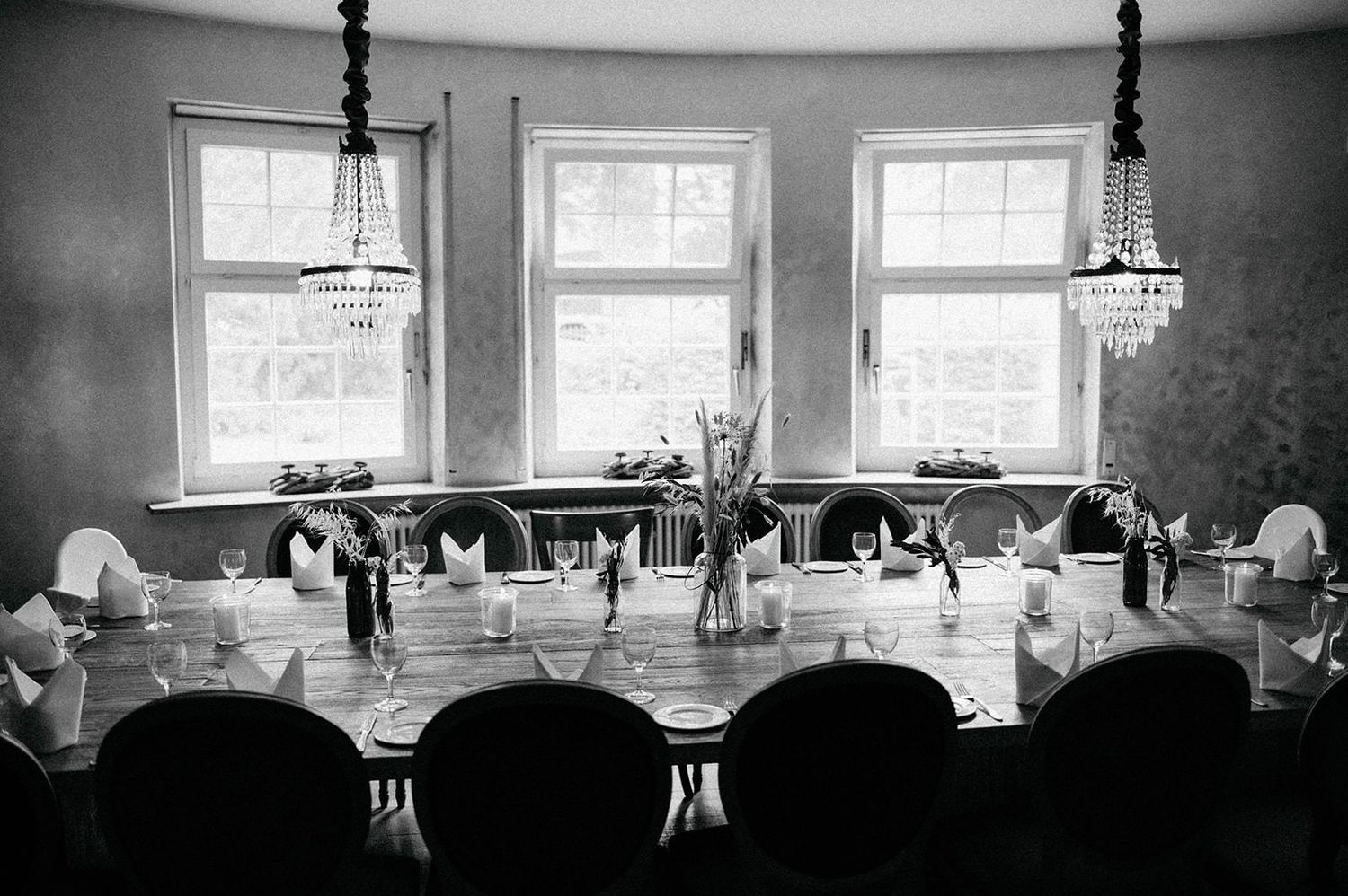 Black and white photograph of an elegant dining room with three windows and a long table set for a formal dinner service.
