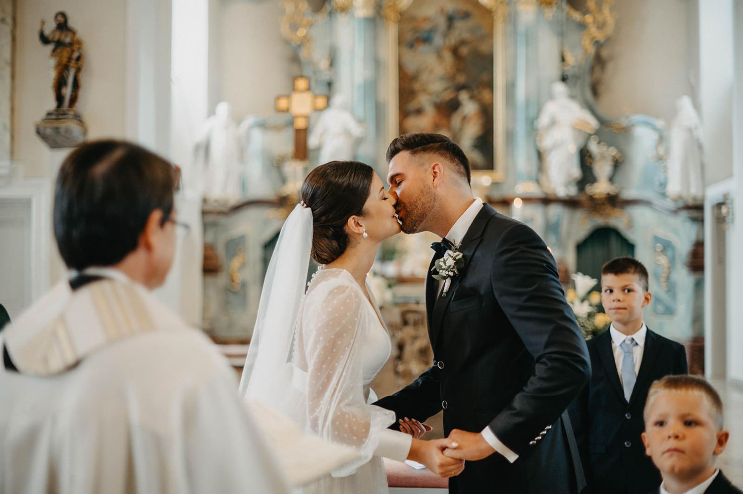 Elegant wedding ceremony taking place in a grand church with ornate architectural details and soft natural lighting.