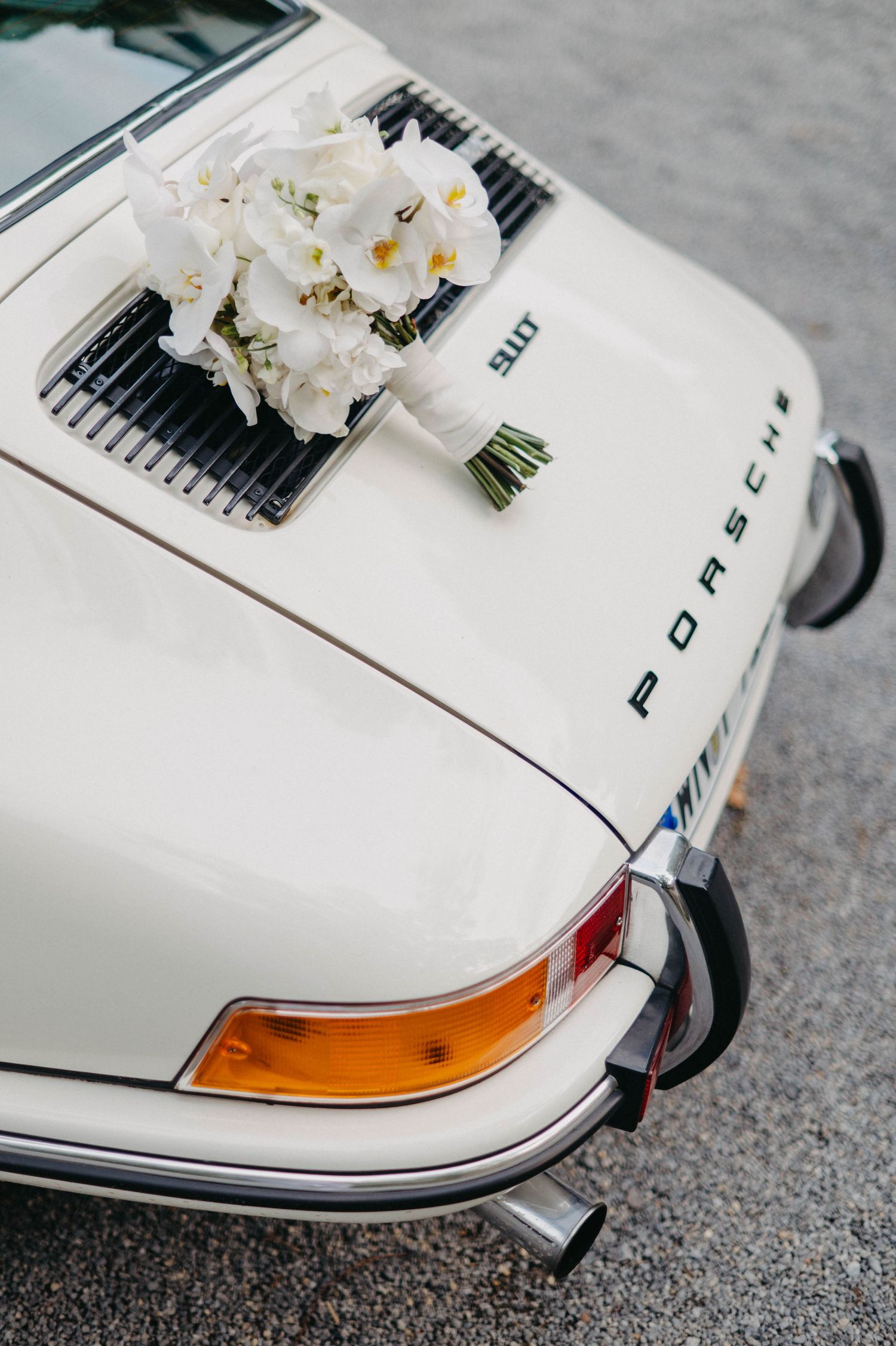 White orchid bouquet resting on hood of classic white Porsche sports car.